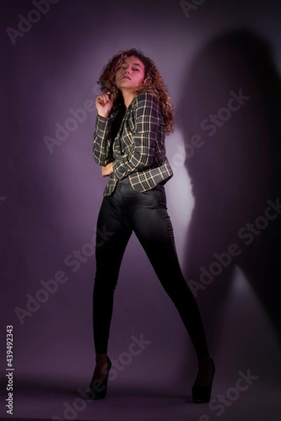 Fototapeta vertical portrait of a curly model wearing a jacket, black pants and high heel shoes in a purple backgroung