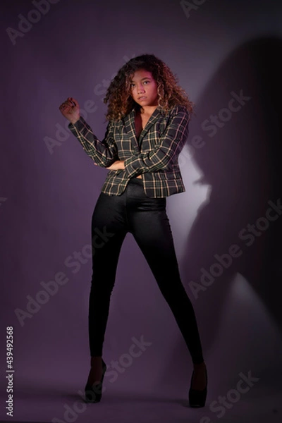 Fototapeta vertical portrait of a curly model wearing a jacket, black pants and high heel shoes in a purple backgroung