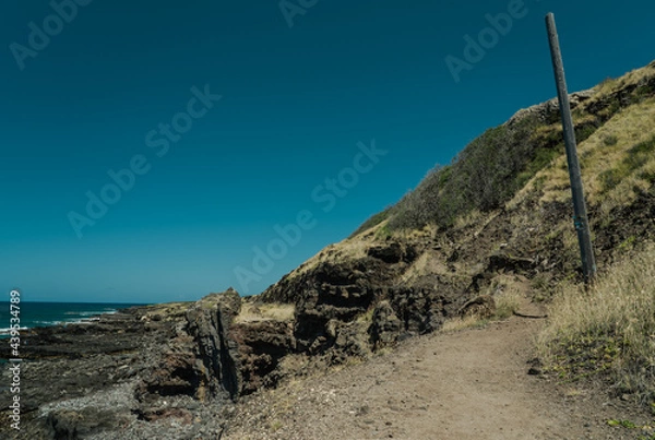 Fototapeta A dike (American spelling) or dyke (British spelling), in geological usage, is a sheet of rock that is formed in a fracture of a pre-existing rock body. Kaena ponit trail, Oahu, Hawaii.