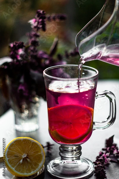Fototapeta Tasty purple basil lemonade in glass with lemon and ice on a dark table in the summer garden. Picnic time with cold drink.