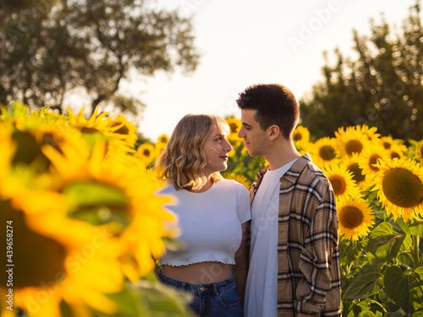 Fototapeta Pareja joven disfrutando de sus vacaciones en un campo de girasoles durante la puesta de sol en verano