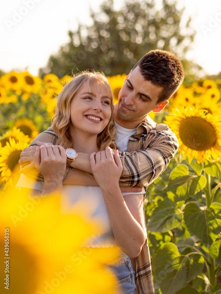 Fototapeta Pareja joven disfrutando de sus vacaciones en un campo de girasoles durante la puesta de sol en verano