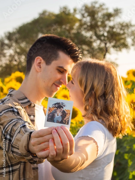 Fototapeta Pareja joven  besándose y sosteniendo una foto polaroid