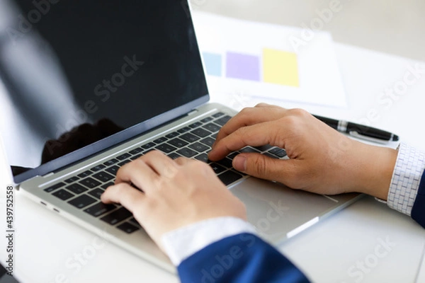 Fototapeta Laptop on office tablen with business man's hand in navy blue suit typing . Concept for cool style workplace