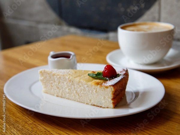 Fototapeta Piece of cheese casserole or cheesecake, garnished with raspberry jam and cup cappuccino coffee on wooden table. Breakfast in cafe, top view, horizontal Traditional russian ukrainian breakfast