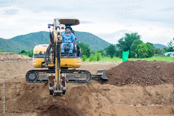 Fototapeta mini excavator digging soil with mountain background