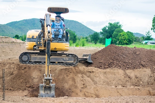 Fototapeta mini excavator digging soil with mountain background