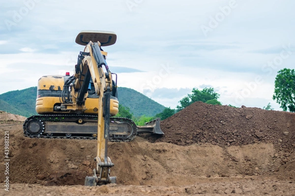 Fototapeta mini excavator digging soil with mountain background