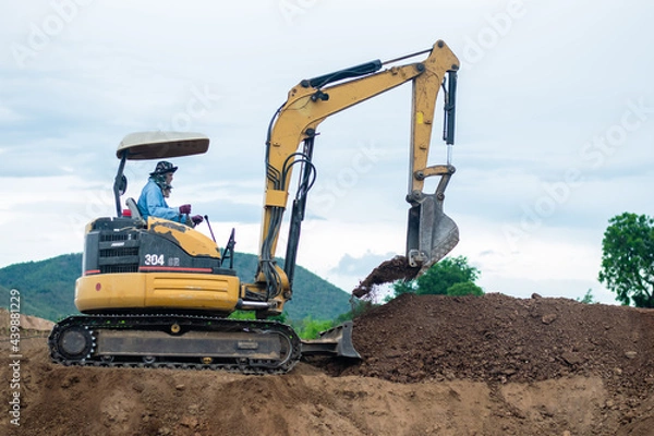 Fototapeta mini excavator digging soil with mountain background
