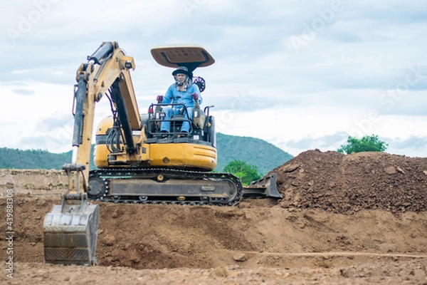 Fototapeta mini excavator digging soil with mountain background
