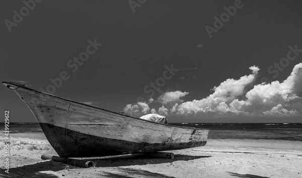 Obraz Dramatic high contrast black and white image of a old weathered wooden fishing boat abandoned on the Caribbean coast in the Dominican Republic. With white sand and cloudy skies.