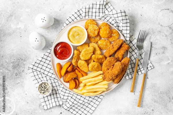 Obraz Chicken nuggets, strips, french fries, fried potatoes, ketchup and cheese sauce on a light background. Fast food top view 