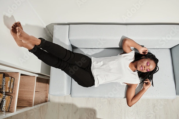 Fototapeta happy african american girl lying on back on sofa resting and dreaming. top view. overhead