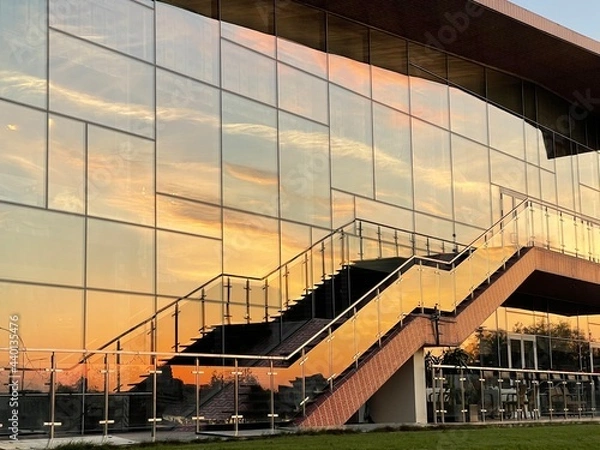 Fototapeta Reflection of the sunset sky in the glass wall of a building with a staircase