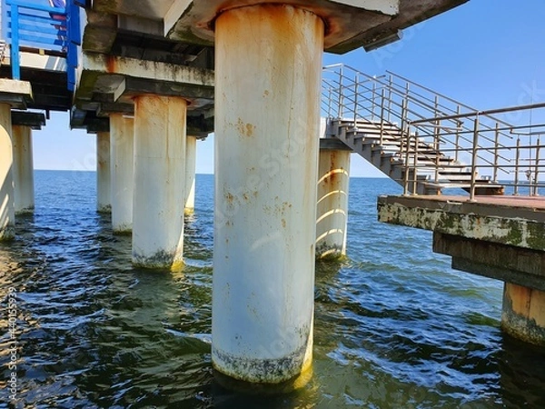 Fototapeta Walkway between concrete pillars.  The walkway to the steps is located between concrete columns on the seashore.