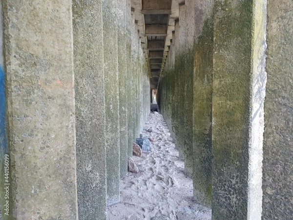 Fototapeta Walkway between concrete pillars.  The path over the stones is located between the concrete pillars on the seashore.