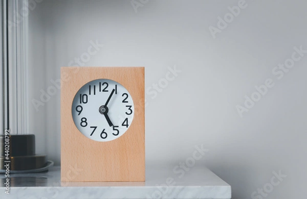 Fototapeta A wooden framed alarm clock sits on the left-hand side on a marble table.