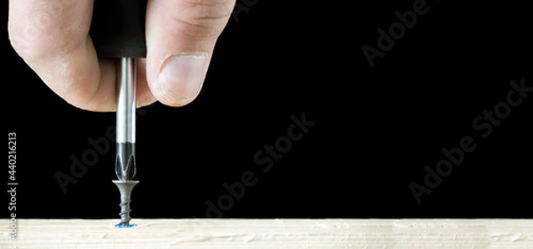 Fototapeta Banner with screwdriver twists the self-cut into wooden boards close up isolated on black background with space for text.