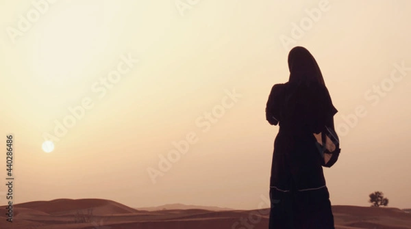 Fototapeta Portrait of a young Arab woman wearing traditional black clothing during beautiful sunset over the desert.