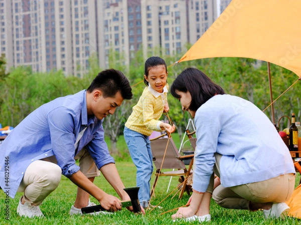Fototapeta A happy family of three set up tents outdoors