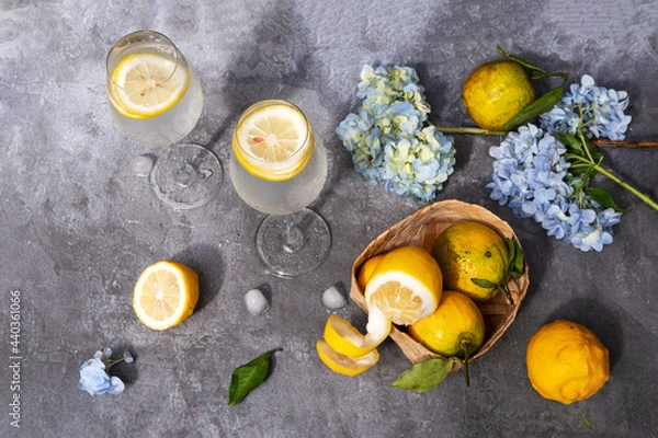 Obraz Water with lemon in glasses, fruits and flowers on a gray concrete background.