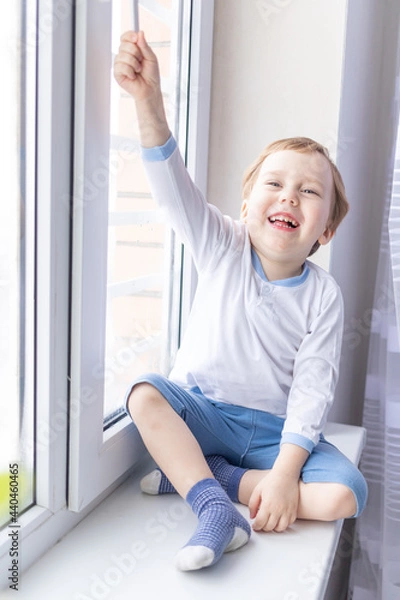 Fototapeta a child boy looks out of the window sitting on the window sill of the house