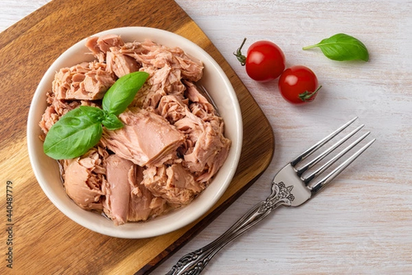 Obraz Top view of canned tuna in a bowl, fork and red cherry tomatoes on a white wooden table. Healthy eating snack of preserved tuna meat and fresh vegetables. Low calories tasty seafood.