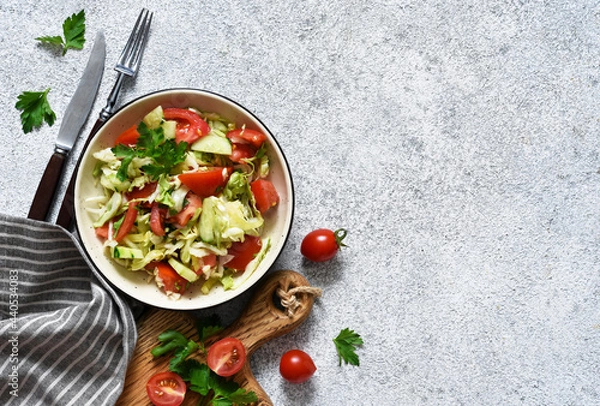 Fototapeta Classic vegetable salad. Salad with cabbage, cucumbers and tomatoes with lemon juice on a concrete background. View from above.