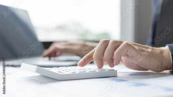 Obraz Businessman presses a calculator to calculate earnings and analyze company earnings in his private office, Information in finance and accounting, Company performance and revenue.