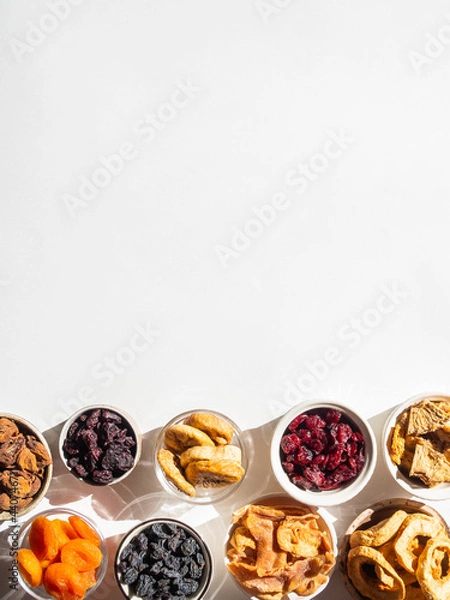 Fototapeta Flat lay various dried fruits and berries in bowls on white background with shadows. Vegan healthy natural snacks.