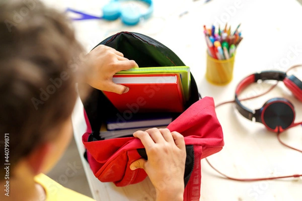 Fototapeta schoolboy puts office supplies in a backpack. Preparing for school. Back to school. Self-assembly of a school backpack. Close-up