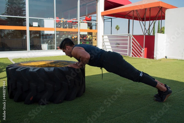 Fototapeta latin or native american men doing push ups in a tire outdoors in front of his gym in a sunny day