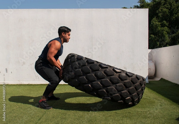 Fototapeta latin or native american man lifting up a tire while he´s doing crossfit outside of his gym in a sunny day