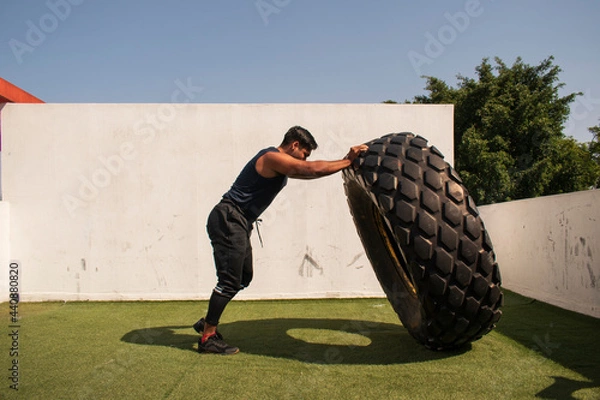 Fototapeta latin or native american man lifting up a tire while he´s doing crossfit outside of his gym in a sunny day