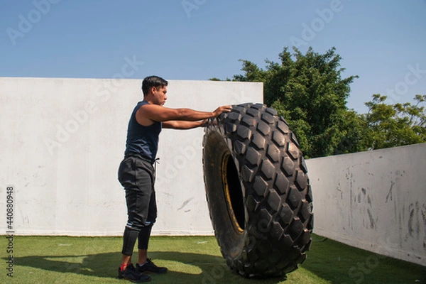 Fototapeta latin or native american man lifting up a tire while he´s doing crossfit outside of his gym in a sunny day