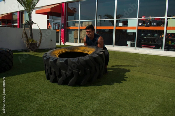 Fototapeta latin or native american man lifting up a tire while he´s doing crossfit outside of his gym in a sunny day