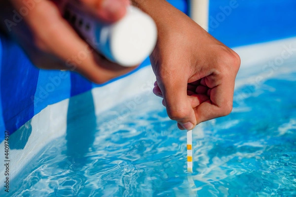 Fototapeta Checking the water quality of a pool with the help of a test strip with PH value, chlorine and algaecide