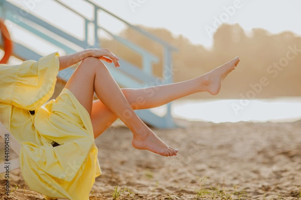Obraz Woman's long slim legs on the sand beach while sunset.