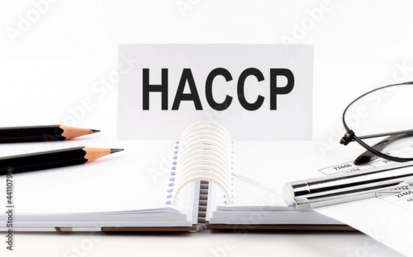Fototapeta Text HACCP on paper card,pen, pencils, glasses,financial documentation on table - business concept