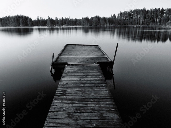 Fototapeta Black and white photo of a jetty at sunset on the Swedish lakes surrounded by forest