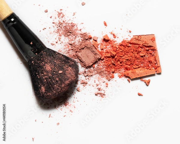 Obraz On a white background is a makeup brush, and next to it is scattered blush. Blush swatches. Decorative cosmetics for women. Make-up products. Loose blush and eye shadow.Cosmetics on a white background