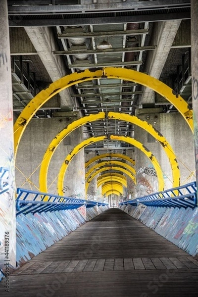 Fototapeta futuristic footpath under a road bridge across the Danube river in Vienna diminishing view