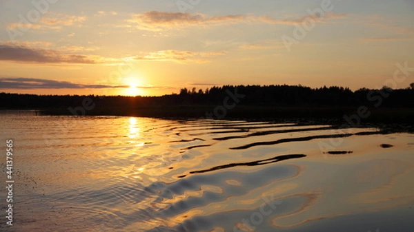 Fototapeta A beautiful orange sunset on the Volga River with a Sun in the sky and a forest on the horizon in the calm water on a summer evening