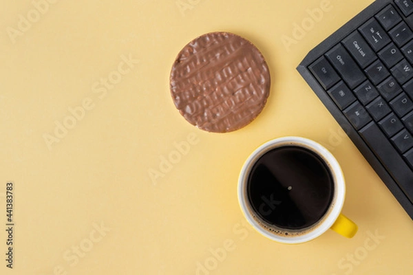 Fototapeta Chocolate cake and coffee nearby keyboard on yellow background. A cup of black coffee or chicory drink and sweet crispy snack for lunch at work.