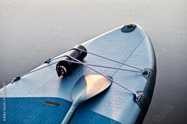 Fototapeta Paddleboard and surf board with paddle on blue water surface background close up. Surfing and SUP boarding equipment in sunset lights close-up. Outdoor water sports. Surfing lifestyle backgrounds.