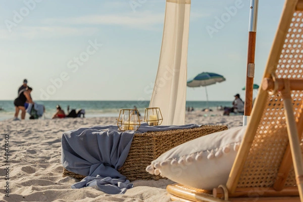 Fototapeta Beach chair with pillow, candles, and a whicker crate box and umbrellas and the horizon in the background