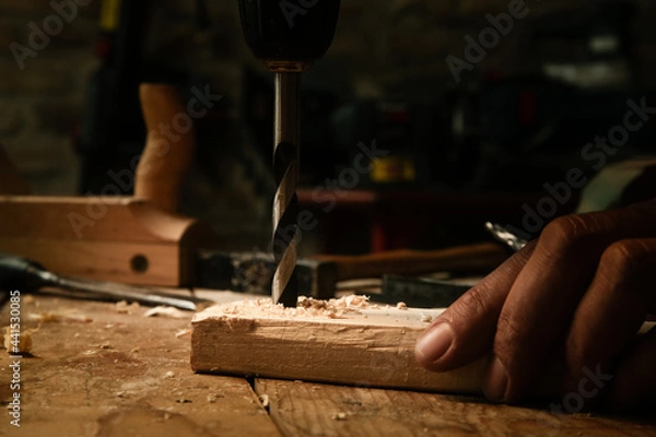 Fototapeta Carpenter using drill machine to make a hole on wooden plank. DIY, woodworking project.