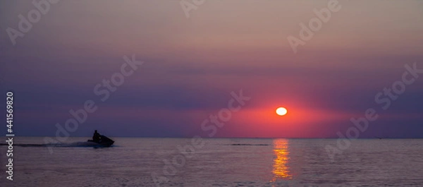Obraz Sunset over ocean with jetski. silhouette of a man on a jet ski in the sun. Jetski at Sunset. Panorama
