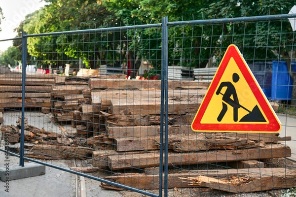Fototapeta Sign of construction work on the background of wooden sleepers. Construction work to replace streetcar tracks in the city. Sign of road works installed on the construction fence in the daytime.