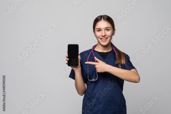 Obraz Beautiful female doctor showing a smart phone screen on a white background